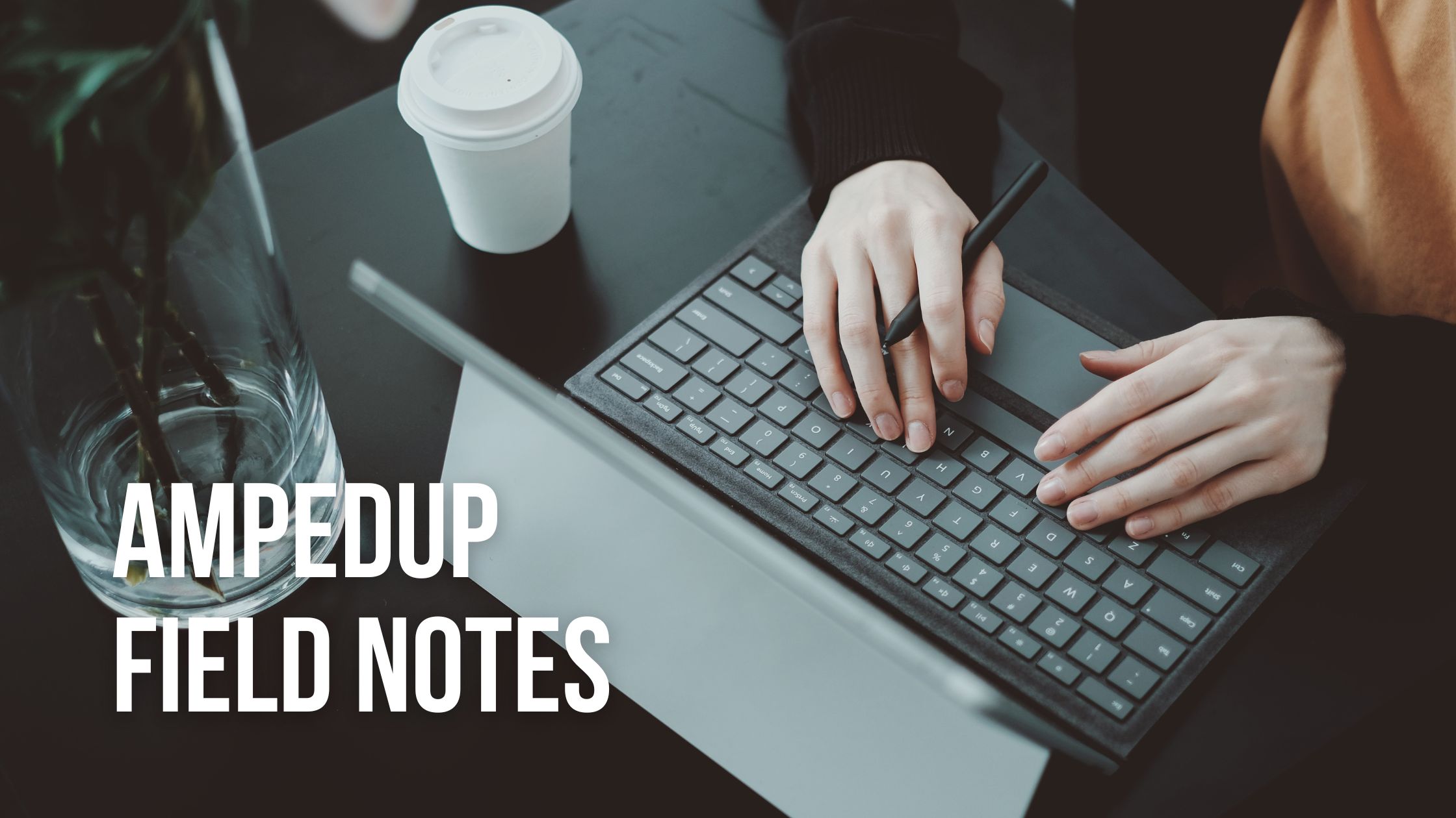 AmpedUp Field notes, Hands over a laptop keyboard typing, with a disposable coffee beside it